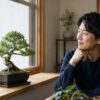 窓辺の盆栽を眺める初心者の日本人男性と明るい室内