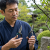 日本庭園でA型とB型の剪定鋏を手に持って比較する日本人男性